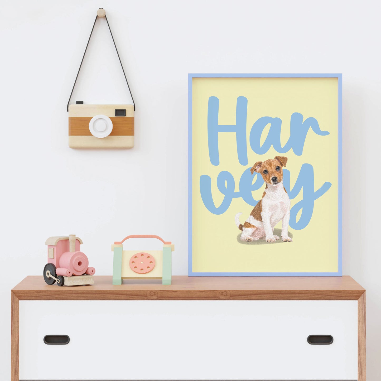 Framed kids pet portrait of a dog with 'Harvey' text on a shelf with toys and a camera.