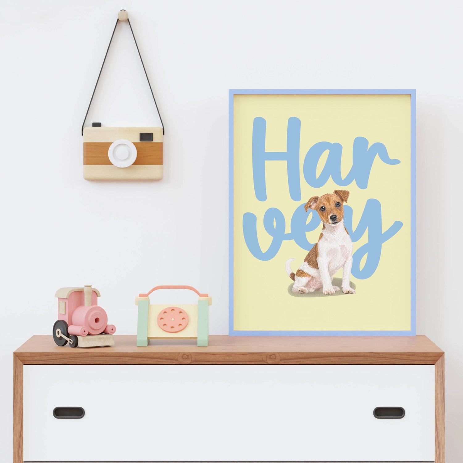 Framed kids pet portrait of a dog with 'Harvey' text on a shelf with toys and a camera.