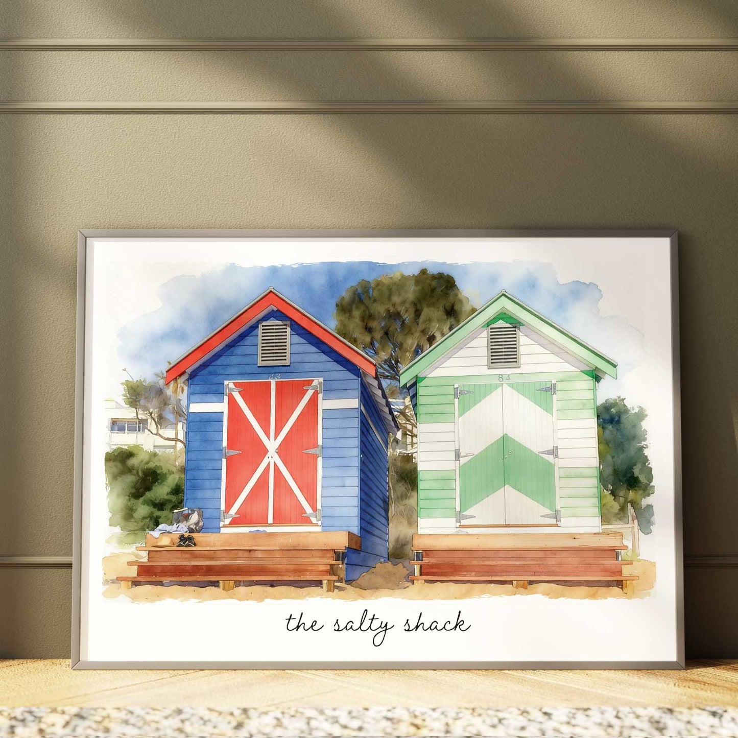 Framed artwork of a custom beach box  portrait with two colourful beach boxes with 'the salty shack' text on a wooden surface.