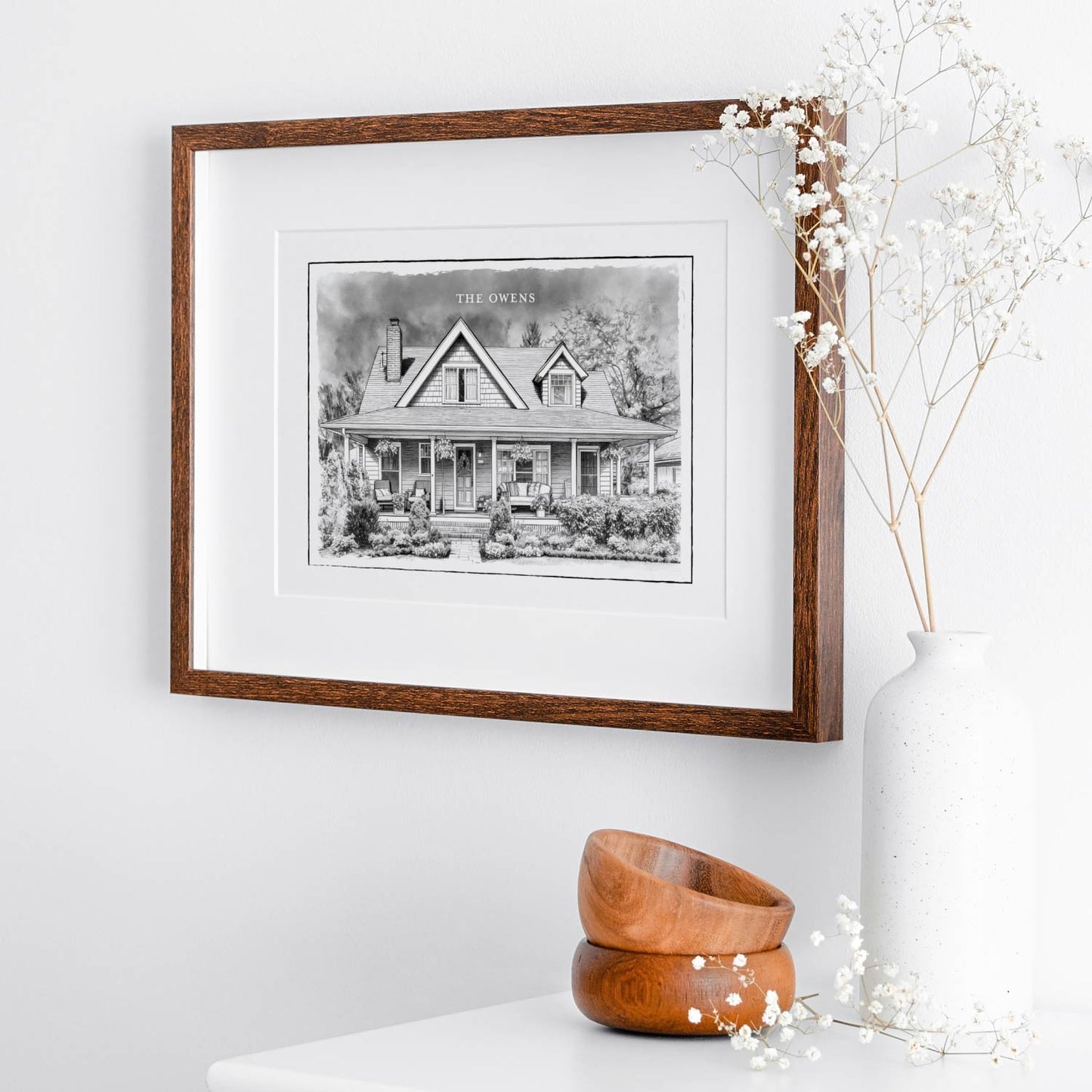 Framed black and white custom home portrait print on a white wall with decorative elements.