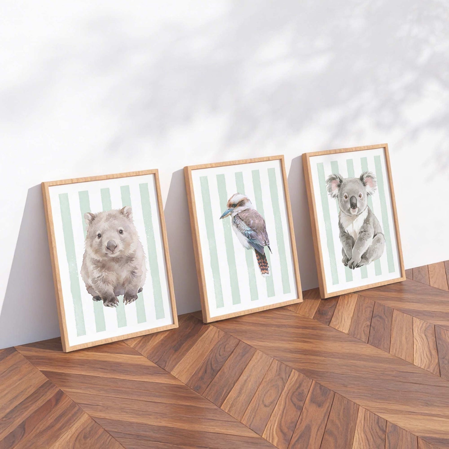 Three framed prints of Australian animals on a striped green background on a wooden floor with a white wall background