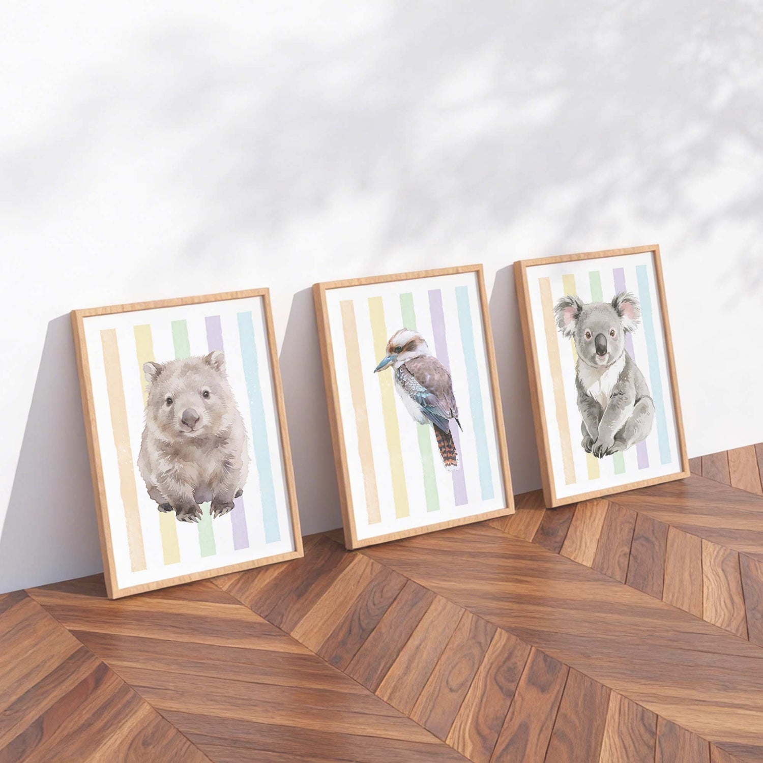 Three framed prints of Australian native animals on a rainbow striped background on a wooden floor with a white wall background