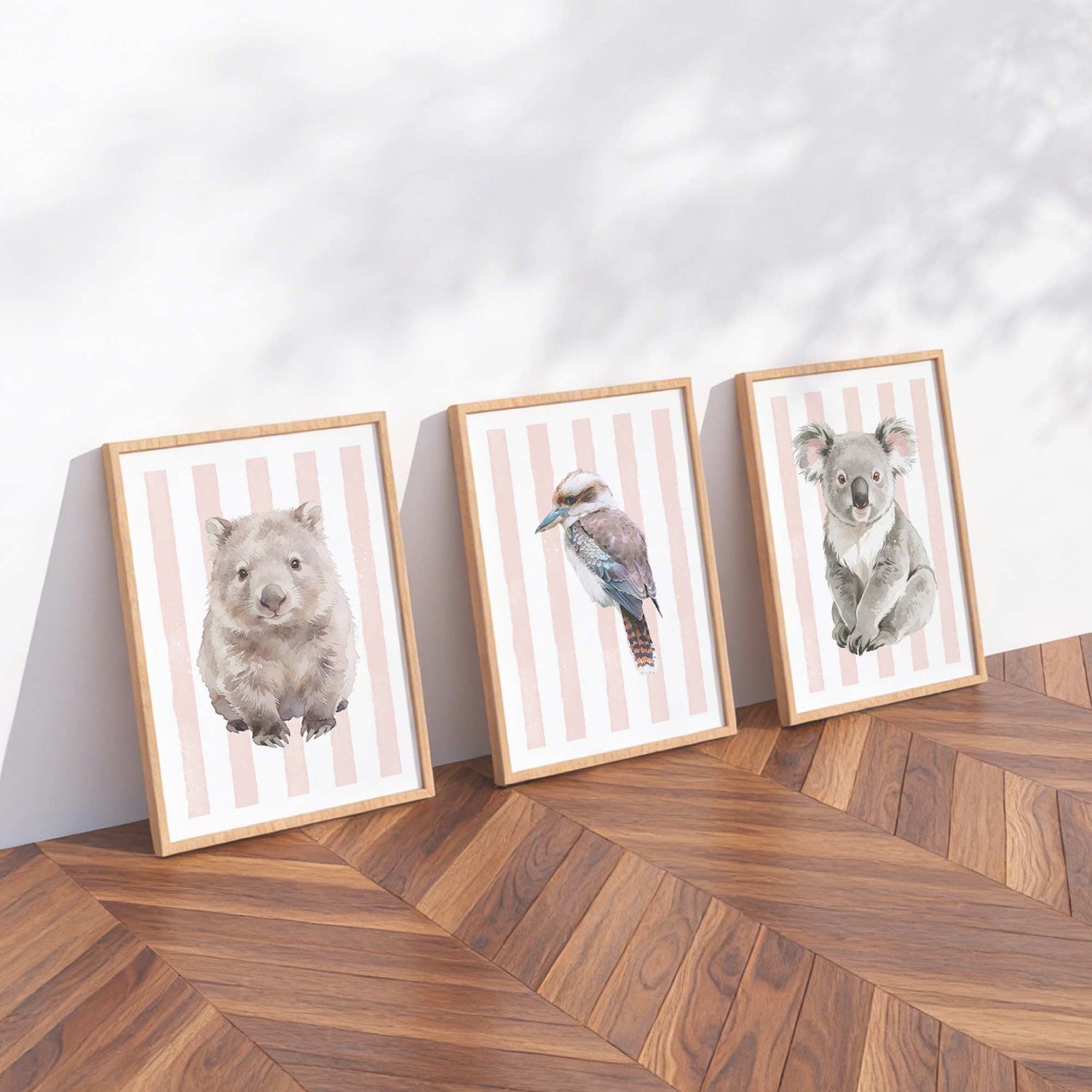Three framed prints of Australian native animals on pink stripes background on a wooden floor with a white wall background