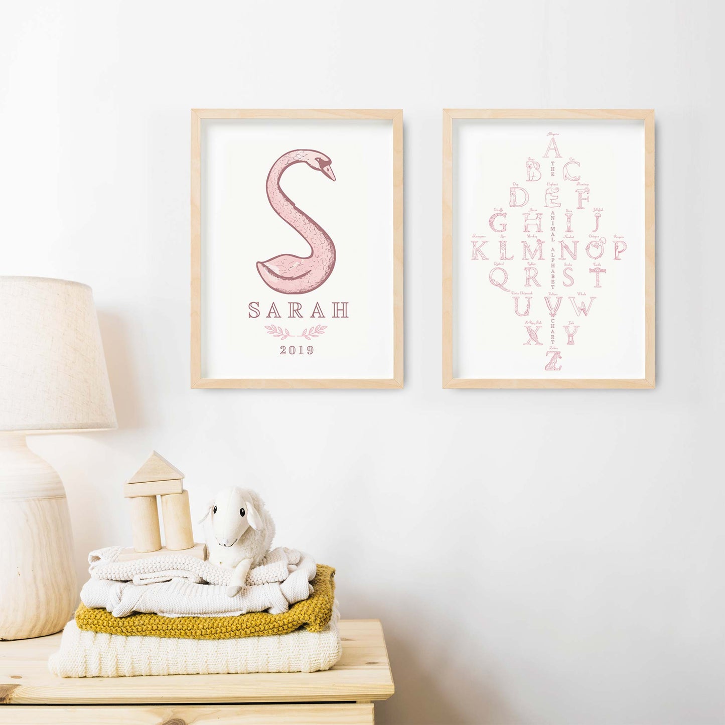 A set of oak picture frames of pink monogram name print and alphabet shape animal chart decorated on the wall of a nursery