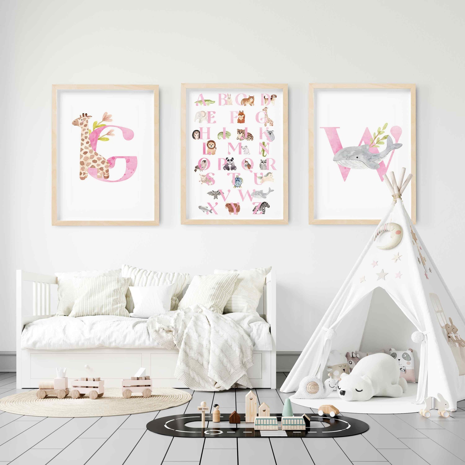 A set of 3 oak picture frames of pink monogram prints and alphabet shape animal chart displayed in a nursery