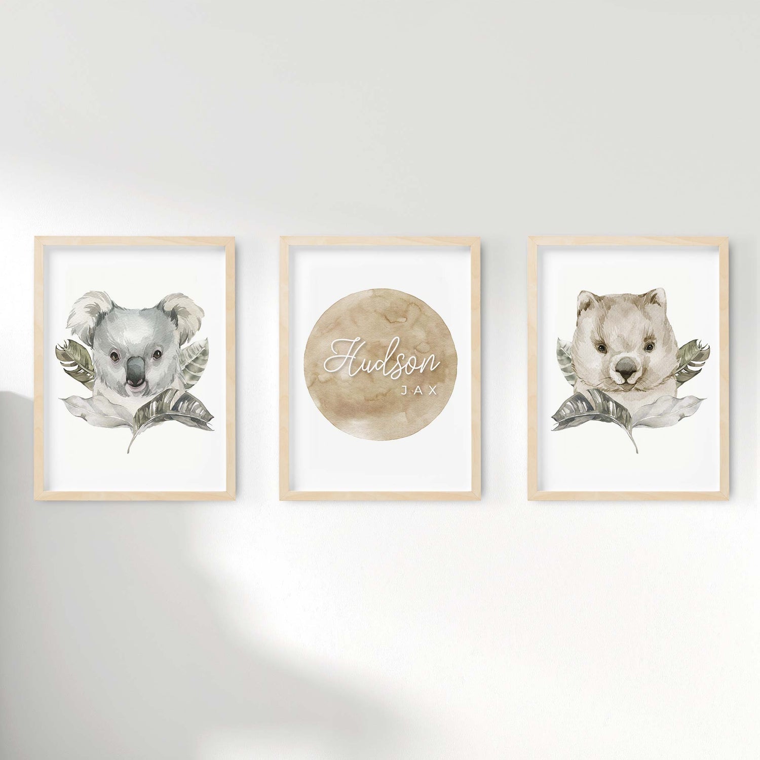 A set of 3 framed oak frames displaying nursery wall prints of Australian wombat and koala behind  individually decorated leaves pairing along with a personalised kids name plaque