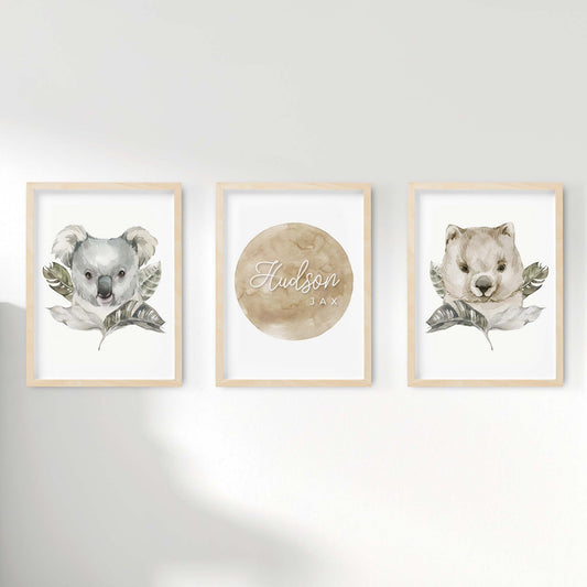 A set of 3 framed oak frames displaying nursery wall prints of Australian wombat and koala behind individually decorated leaves pairing along with a personalised kids name plaque