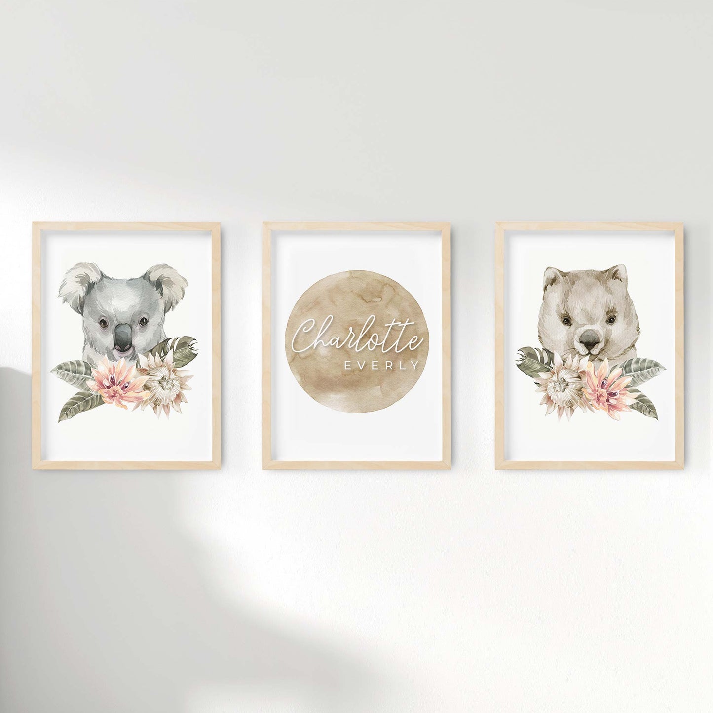 A set of 3 framed oak frames displaying nursery wall prints of Australian wombat and koala displayed behind floral centerpieces pairing along with a personalised kids name plaque 