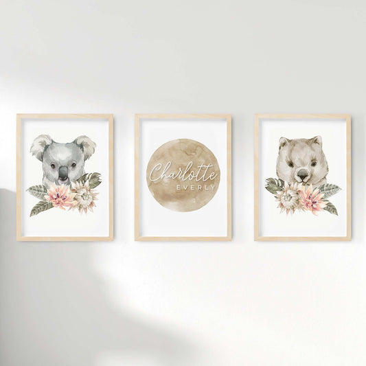 A set of 3 framed oak frames displaying nursery wall prints of Australian wombat and koala displayed behind floral centerpieces pairing along with a personalised kids name plaque