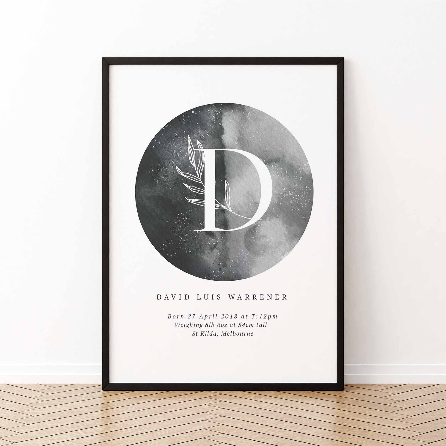 A black picture frame of a grey moon with a botanical letter monogram and personalised birth print details 