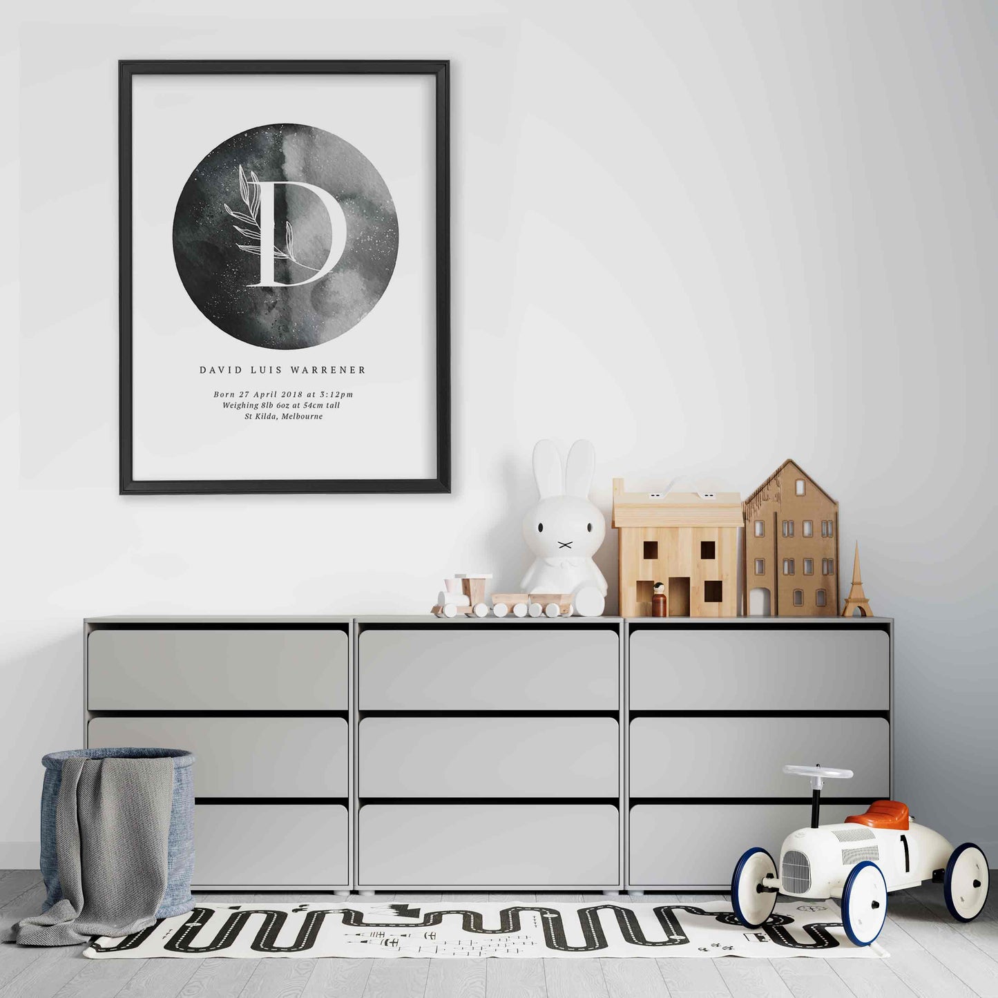 A black picture frame of a grey moon with a botanical letter monogram and personalised birth print details in a boy's bedroom