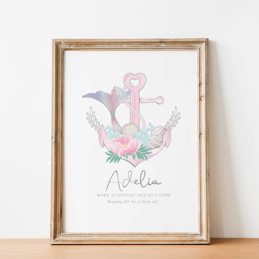 An oak frame with a picture of a pink nautical birth print featuring an anchor, mermaid tail, seashells, string of pearls and floral details