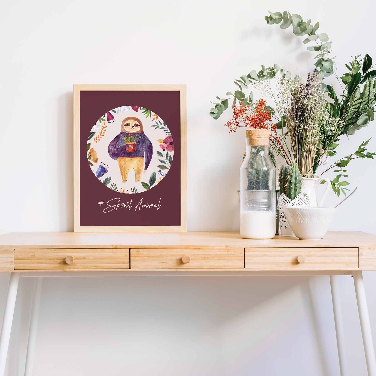 A oak frame picture of a cute sloth floral aspirational kids print on a table