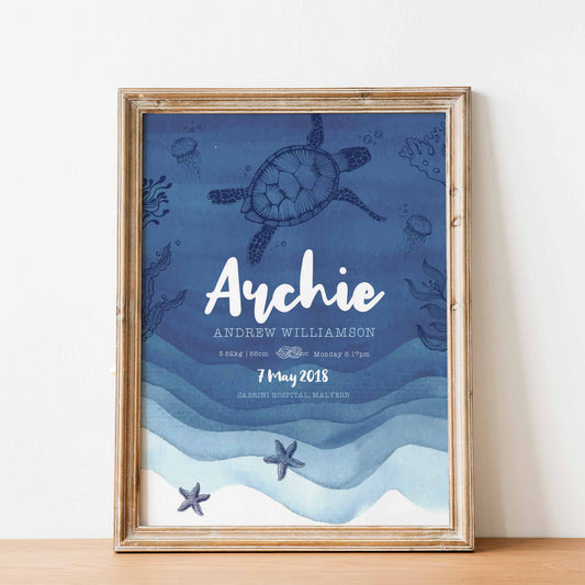 An oak framed  picture frame of a blue nautical birth print featuring a turtle, jellyfish, star fish swimming under the sea