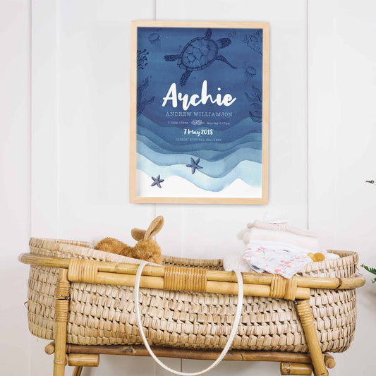 An oak framed picture frame of a blue nautical birth print featuring a turtle, jellyfish, star fish swimming under the sea decorated in a baby's nursery